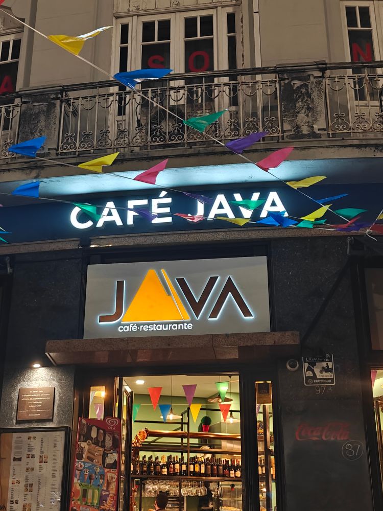 Café entrance with the second floor of a building visible with several windows at night. Logo and name "Café Java" and "Java" between the door and windows above.