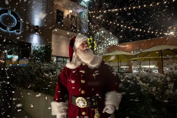 Santa is wearing a red and white suit and watching the falling snow. https://www.nytimes.com/2022/12/23/upshot/santa-job-christmas.html