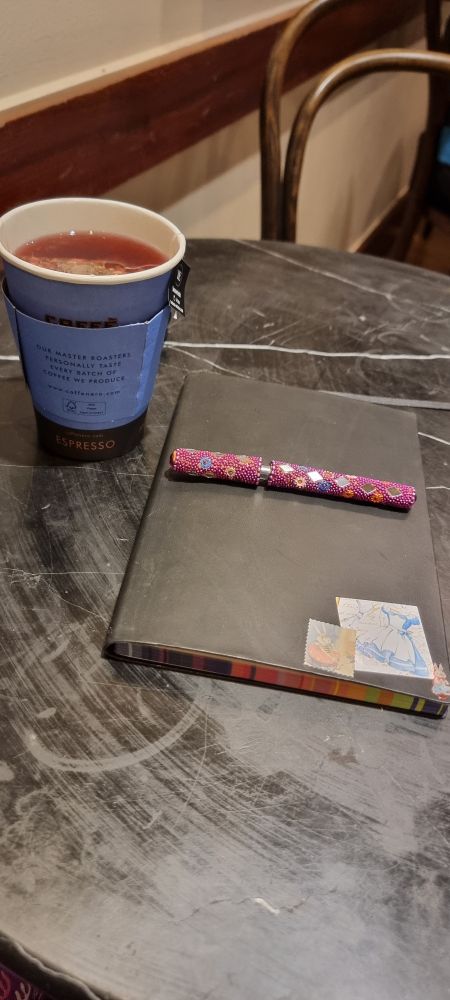Tea, a notebook and a pen on a round black marble table.