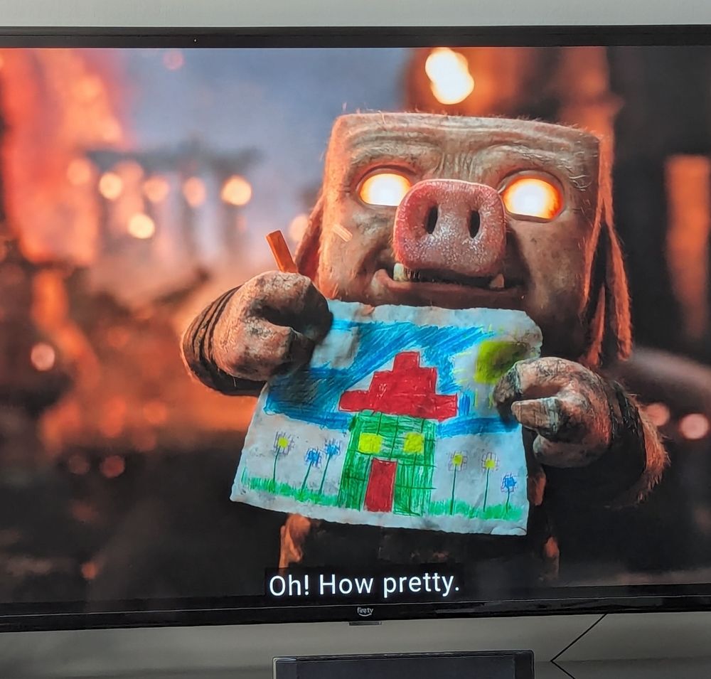 A young piglin from A Minecraft Movie. The creature, a blocky pig-man, stands in the Nether, a fiery hellscape filled with ruins, proudly holding a picture he has drawn in crayon of a blocky house surrounded by flowers.