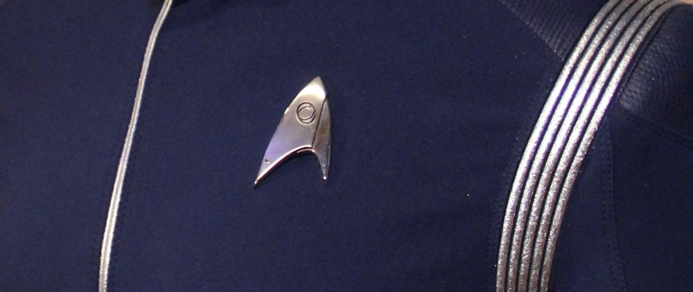 An image of the Starfleet Delta worn on Michael Burnham's "consultant" uniform in Season 1 of Star Trek Discovery. It is a stylised arrowhead and is asymmetrical, with a bigger corner on the left than on the right. It is silver, matching the decorations on the uniform, and features a stylised eye, representing Science.

On Star Trek maps, the Alpha Quadrant is usually depicted on the left of a meridian line that runs through Earth.