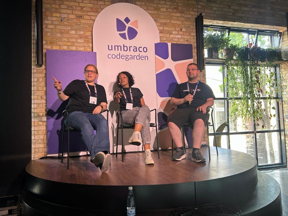 A small stage in front of an Umbraco Codegarden sign, with hosts Lotte and Emma sitting alongside guest Andy Boot