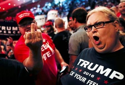 Two Trump fans at a trump 2016 rally demonstrating their commitment to free speech by wearing t-shirts that say "fuck your feelings". The woman is yelling something while the guy flips off the camera.