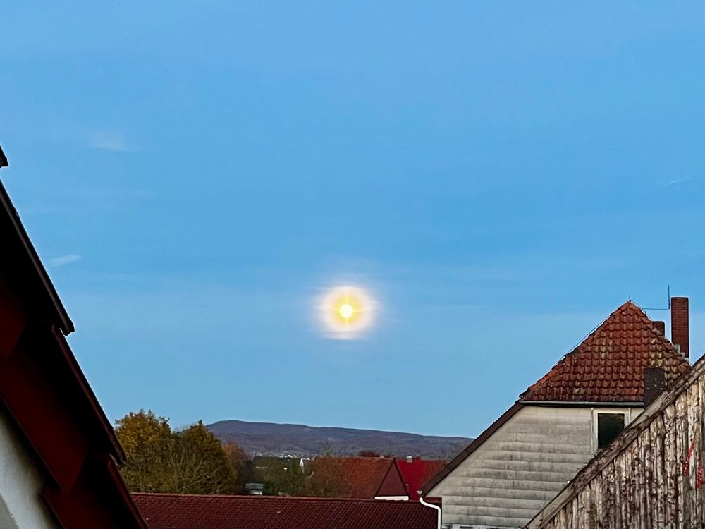 Der Mond, durch die Kameraeinstellungen sieht er aus wie ein Stern, zwischen Häusern 