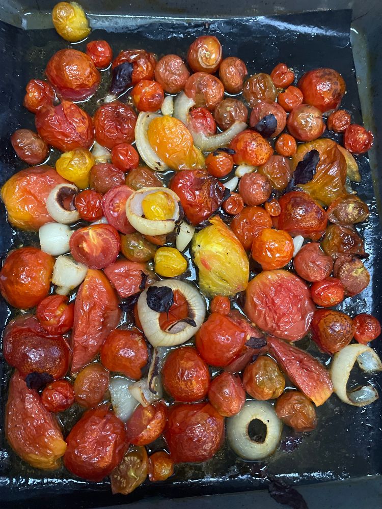 A sheet pan with roasted garden tomatoes, garlic, onions, and purple basil 