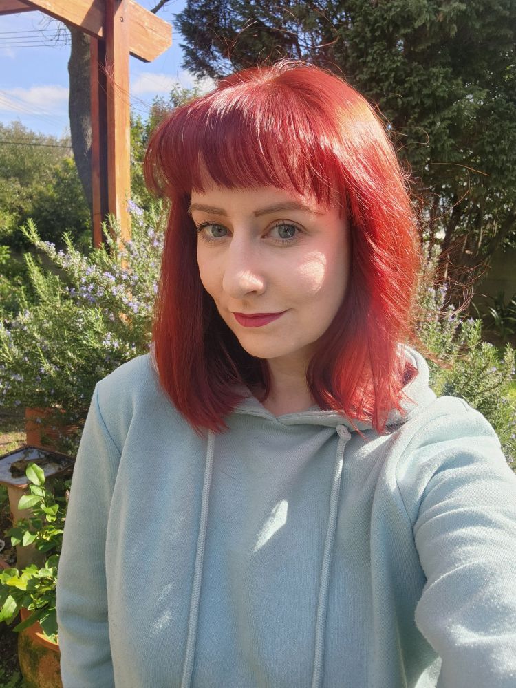 Selfie of a white femme person with shoulder length red hair