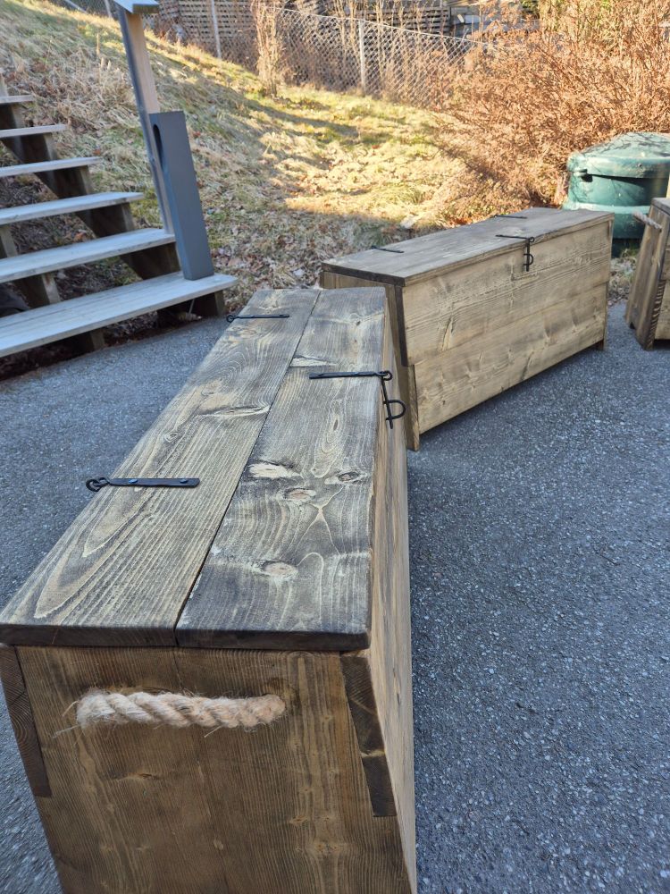 Same chests from the side, dark brown wood with rope handles. 