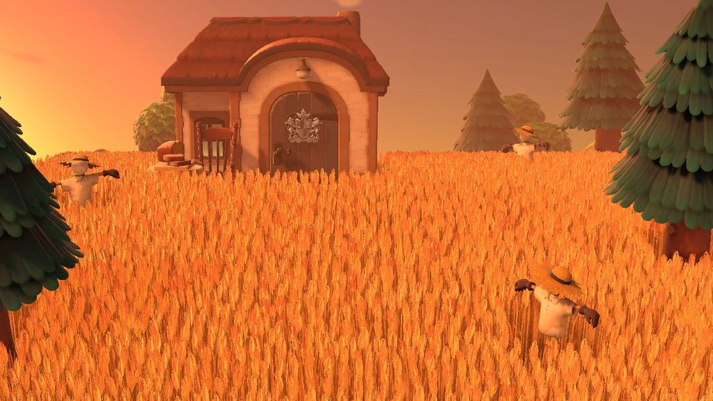 A view of a villager’s home nestled in a golden wheat field in Animal Crossing: New Horizons. It’s dotted with trees and scarecrows