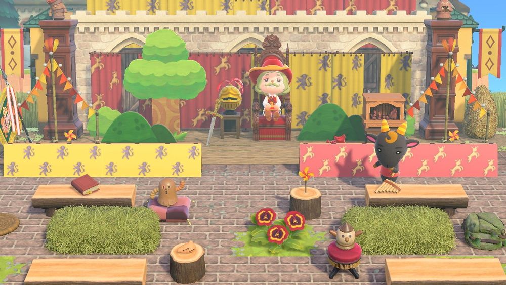 A jubilant medieval stage in Animal Crossing: New Horizons. It’s decorated with vibrant coat of arms tapestries, tree standees, and props. A mustachioed troubadour and the goat villager Nan are also pictured.