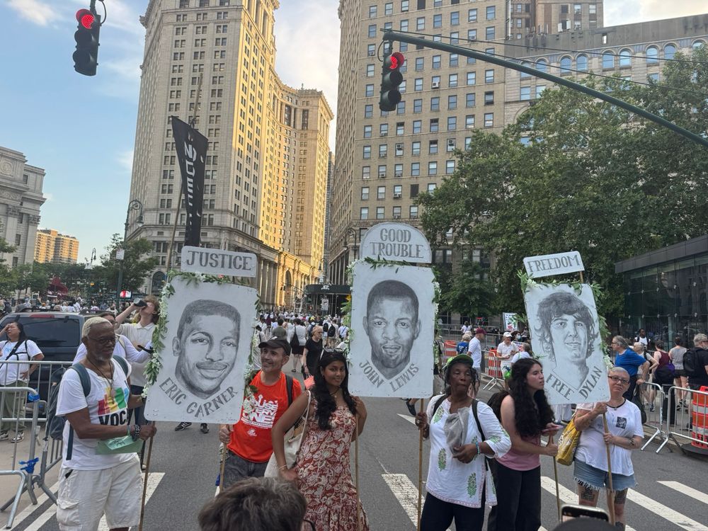 People holdings signs with portraits of Eric Garner, John Lewis, and Dylan Lopez Contreras.