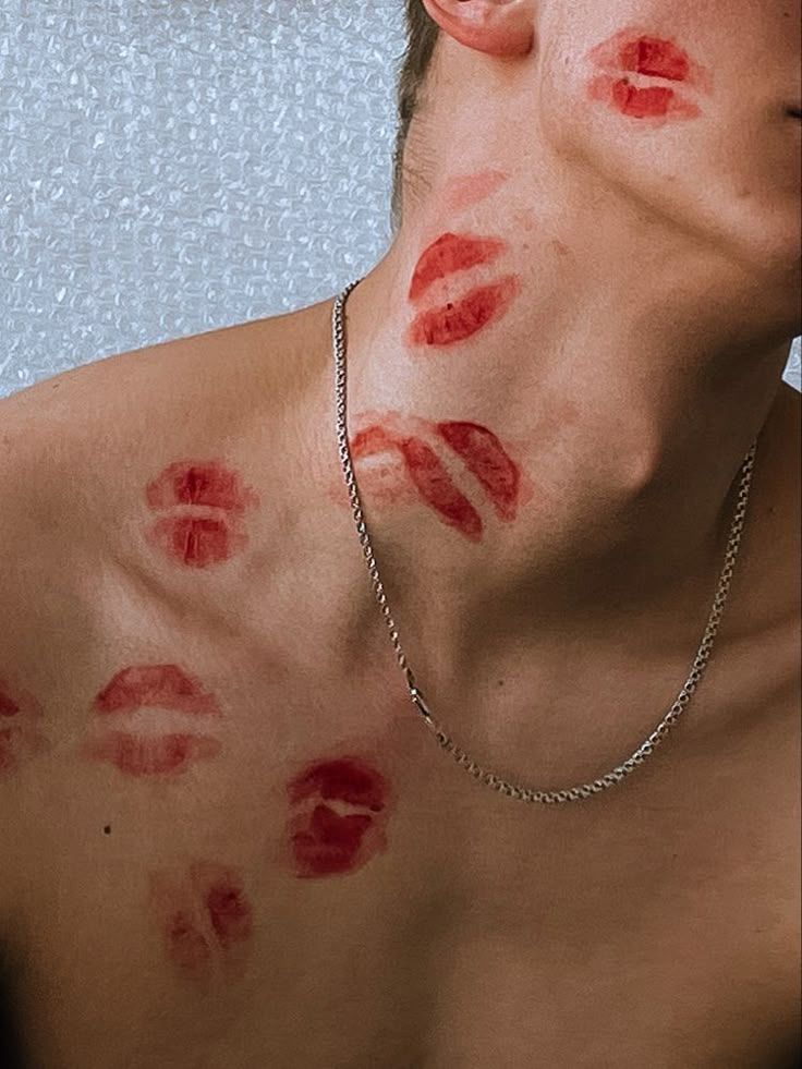 Photo of a man's chest, collarbone, neck, and cheek peppered in red lipstick kiss marks