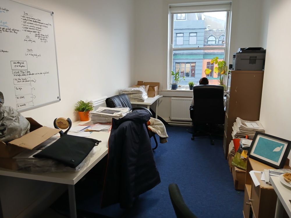 Our one-room office, with four desks, a window at the end, and piles of newspapers everywhere.