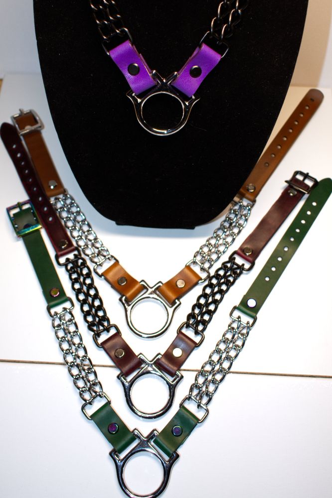 Four leather collars with a bridle ring at the center. The collars are purple whiskey brown, chocolate brown, and green. Other colors not pictured
