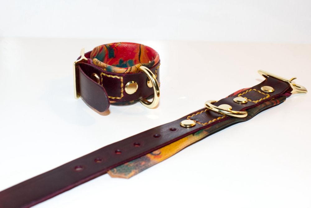 A pair of wine red leather cuffs with the butterfly floral backing. One cuff is laid flat, the other is cinched