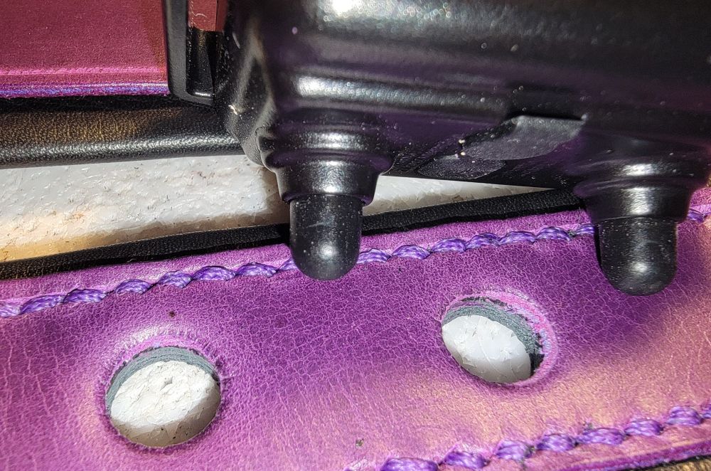 A close up shop of a leather project showing a black object sitting on top of purple leather that's been stitched into leather padding and had 2 holes cut out