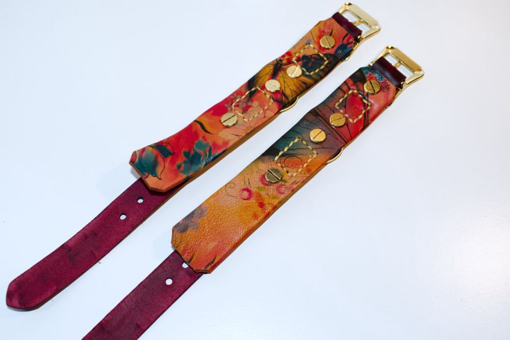 A pair of wine red leather cuffs with the butterfly floral backing. both are laid upside down to highlight the floral backing