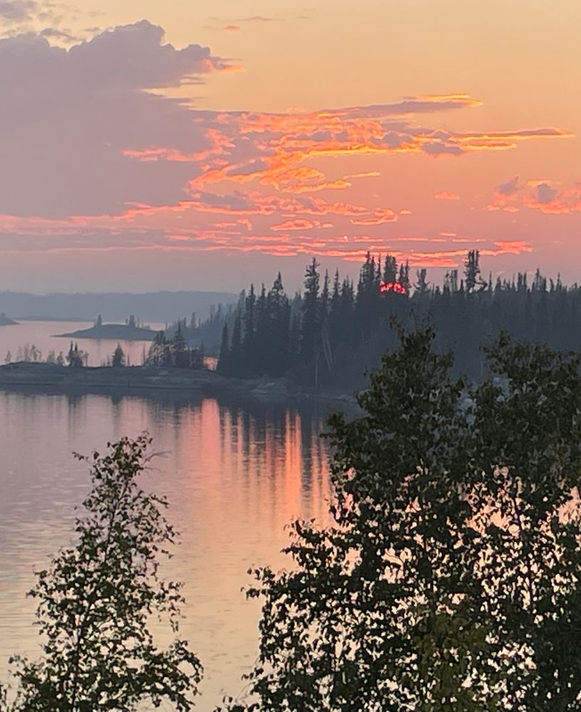 Red glowing sunset over a lake surrounded by spruce forest. 
