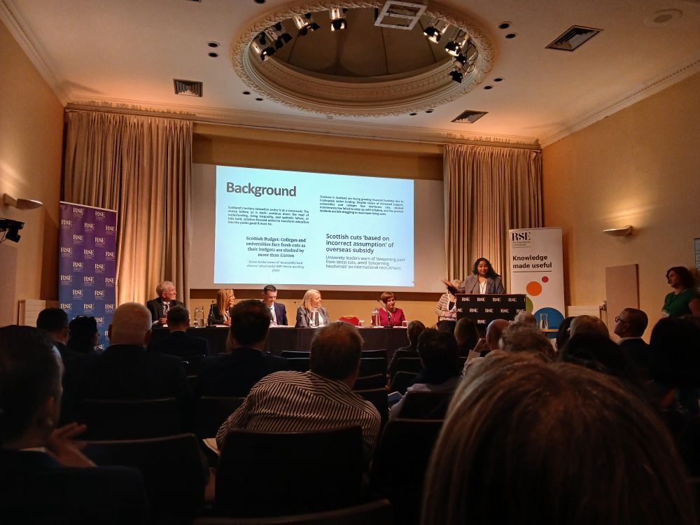 An image of the lecture hall in the Royal Societ of Edinburgh. NUS Scotland President Sai is addressing the room from stage where she sits on a panel on the future of Scotland’s tertiary education.