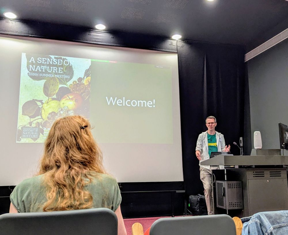 The president of the SHNH, Jack Ashby, standing at the front of a lecture theatre with an opening 'welcome' slide on the screen behind him.