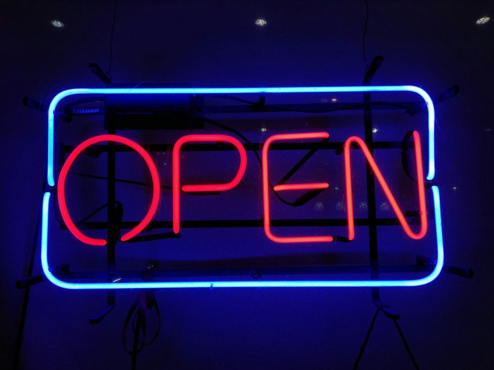A neon sign displaying the word 'OPEN' in bright red letters, outlined by a rectangular blue neon border, mounted against a dark background.
