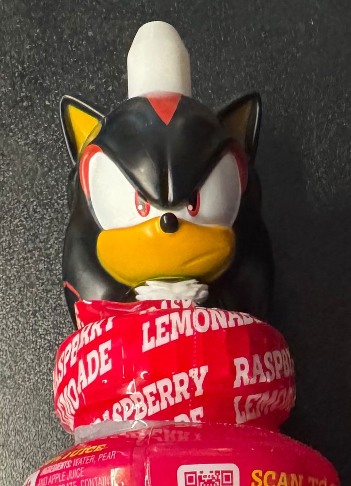 A plastic bust of Shadow the Hedgehog mounted to a raspberry lemonade drink lid. The straw appears to go through his head. He looks very grumpy about this fact. 