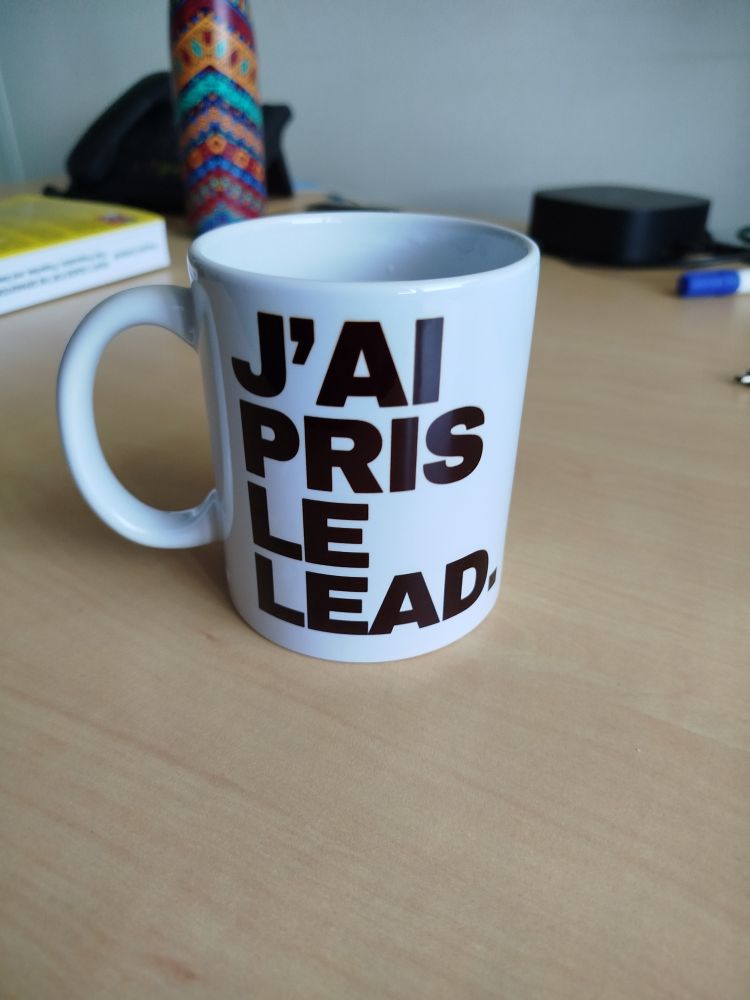 Mug blanc sur lequel il est écrit en noir "J'ai pris le lead."