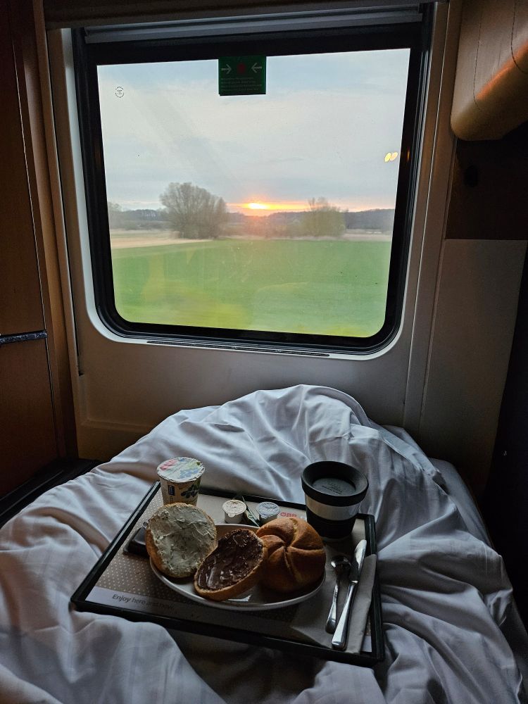Breakfast in bed, in front of a train window with sunrise outside.