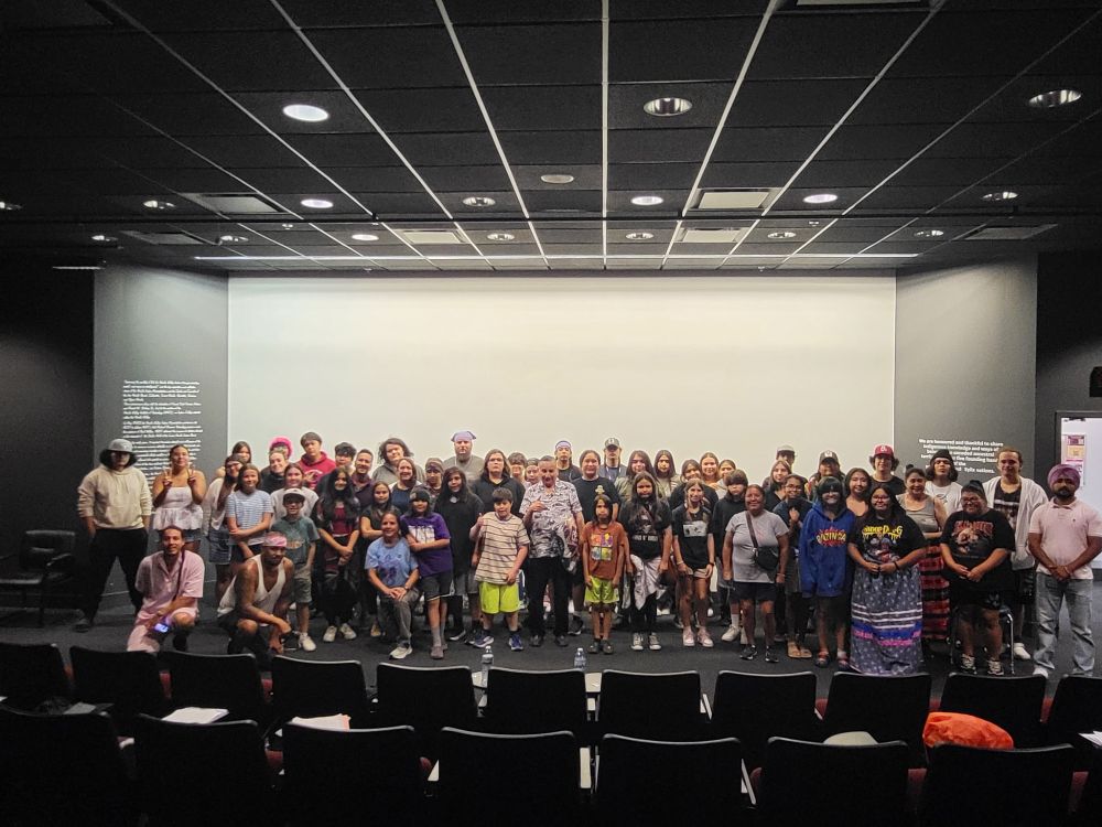 Grand Chief Stewart Phillip in center of photo on a stage, surrounded by Indigenous youth. 
