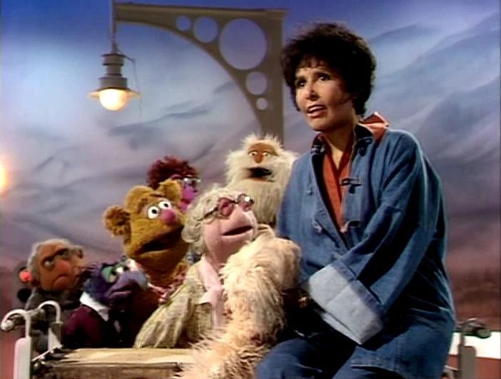 Lena Horne in a denim jumpsuit holding Muppy singing I Got a Name while a chorus of Muppets including Hilda, George the Janitor, Fozzie and Gonzo accompany her