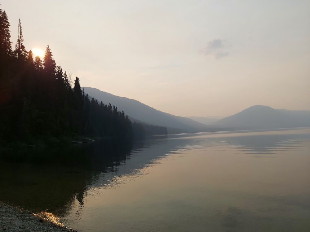 Silhouette of trees and misty lake, mountains in horizon.