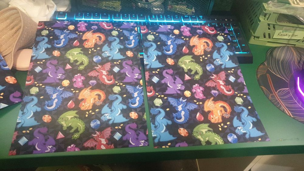 Photograph of a print out of a repeating pattern of rainbow dragons and gemstones on black background