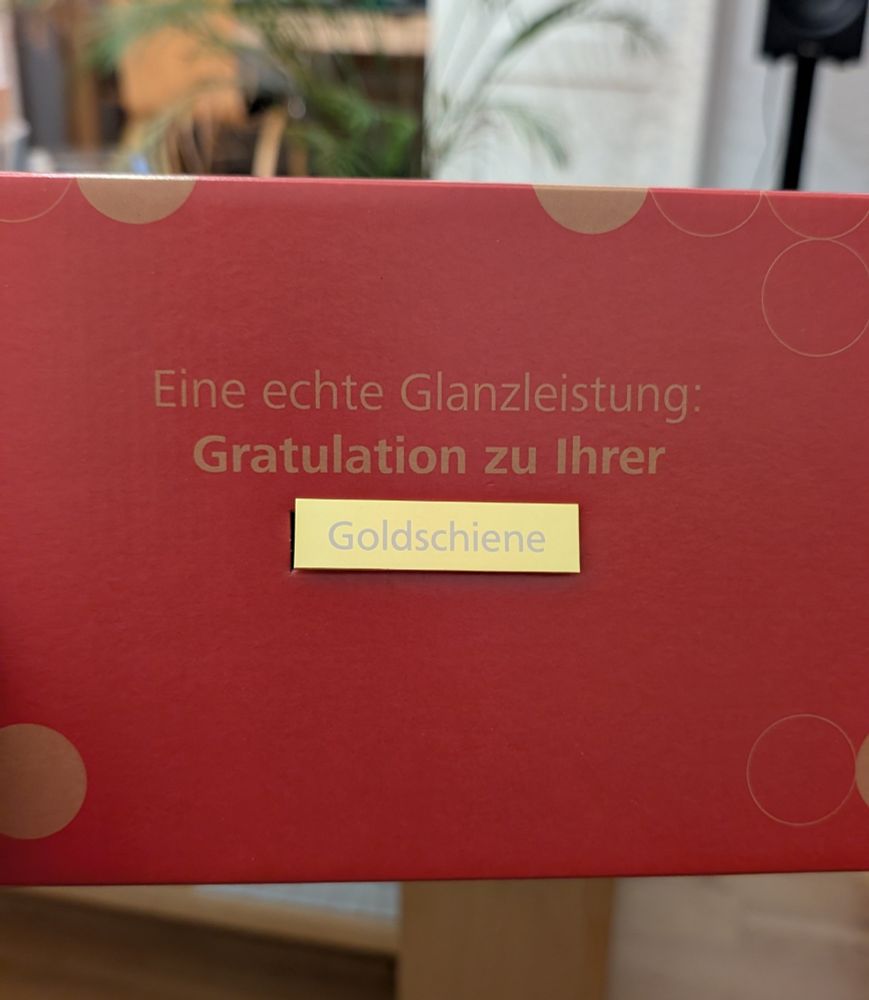 Eine rote Box mit goldener Schrift: Eine echte Glanzleistung. Gratulation zu Ihrer Goldschiene
