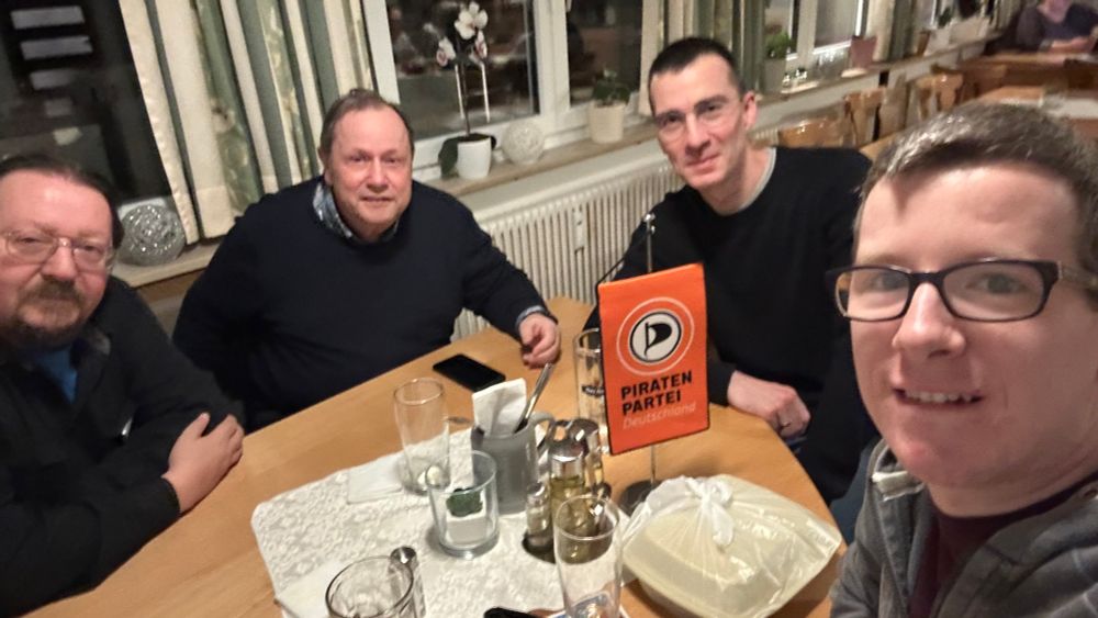 Vier Männer sitzen an einem Tisch in einem Restaurant und schauen in die Kamera.