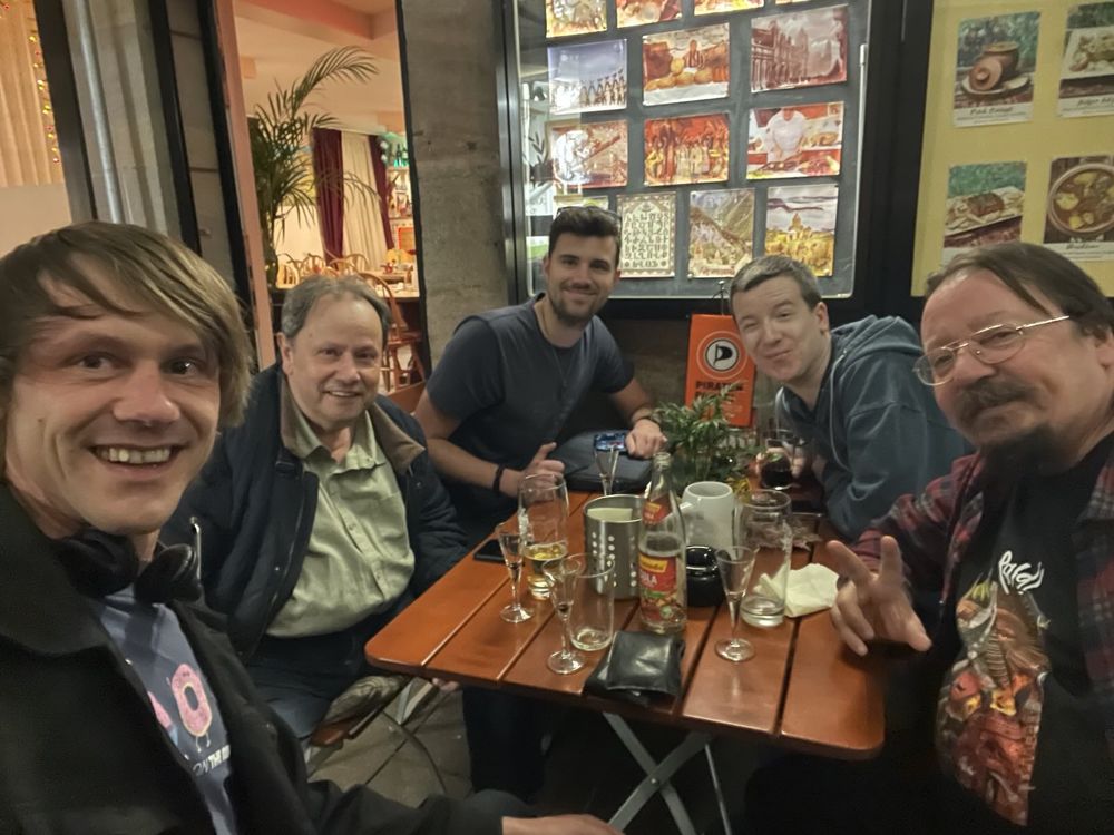 5 Personen sitzen an einem Tisch im Restaurant und schauen in die Kamera. Es stehen Gläser auf dem Tisch.