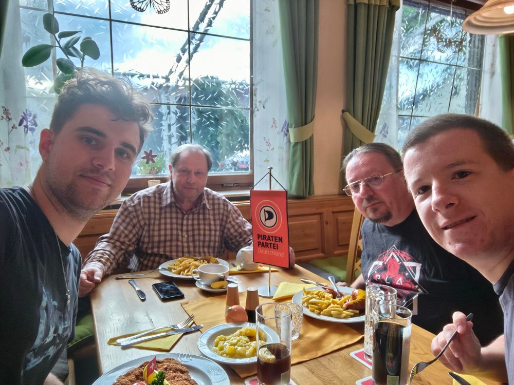 Vier Personen sitzen an einem Tisch in einem  Restaurant und es steht Essen und Getränke auf dem Tisch. 