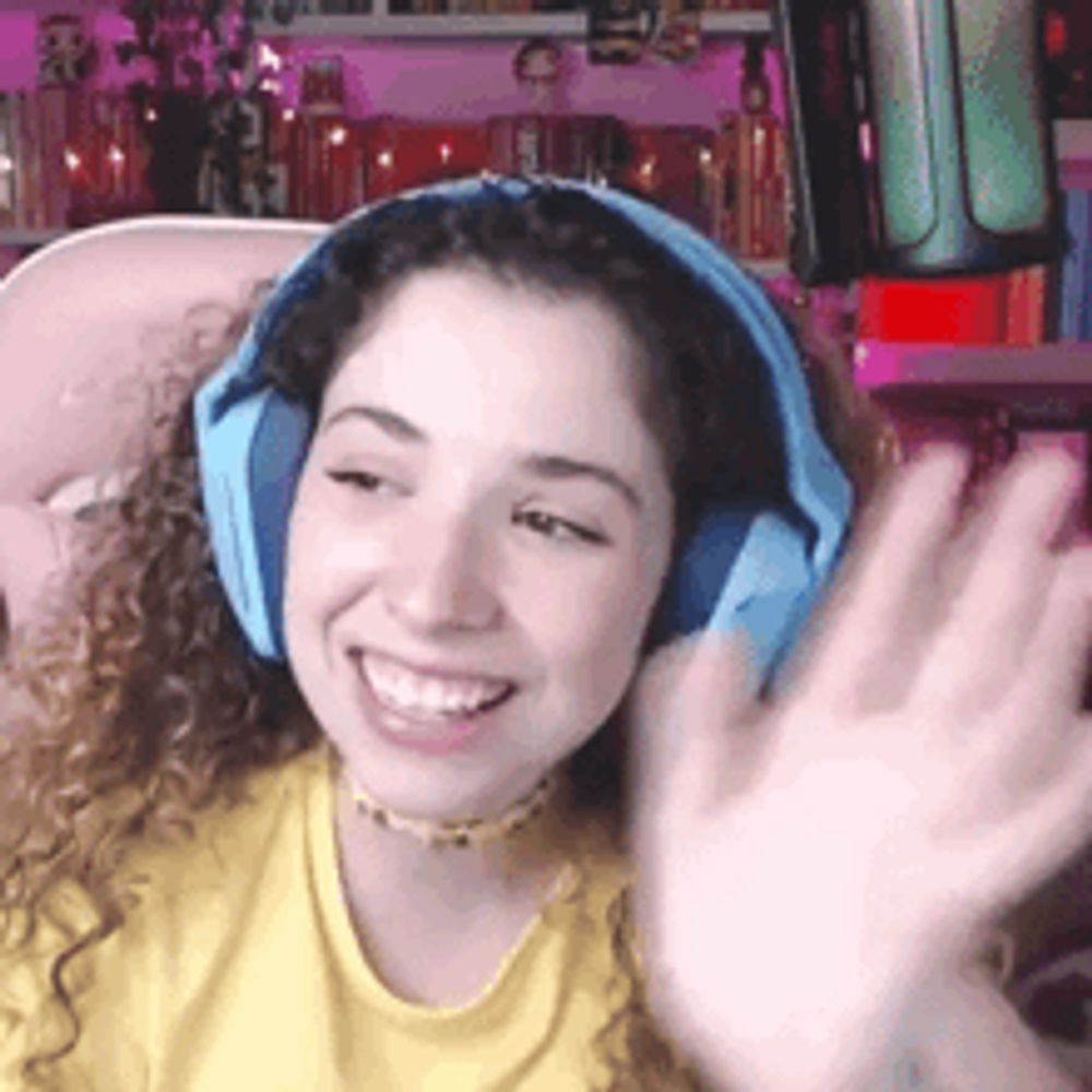 a woman wearing headphones and a yellow shirt is smiling and waving