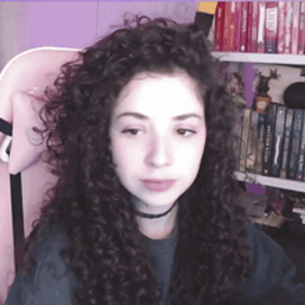 a girl with curly hair is sitting in front of a bookshelf with a book titled dune