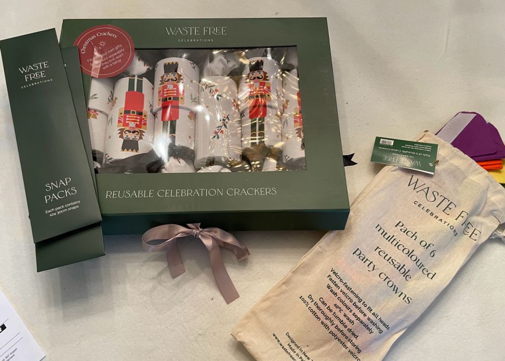 Green storage box of nutcracker-fabric-covered Christmas crackers, paper packet of snaps and cloth bag of cotton crowns to fill crackers