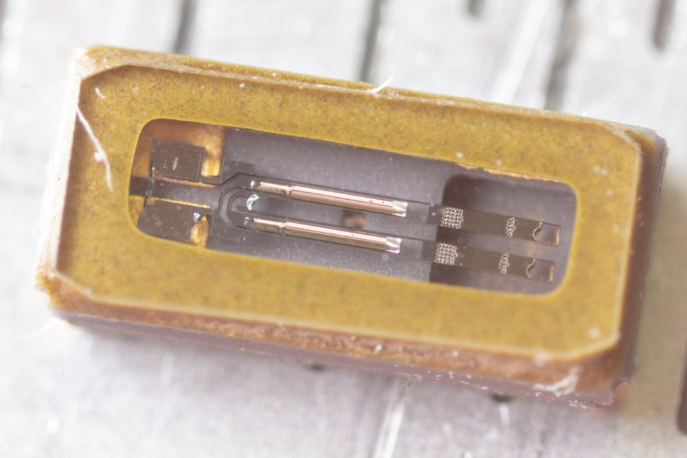Macro photo. A surface mount 32.768kHz crystal component a glass top of the components shows the internals. A tuning fork structure is visible.