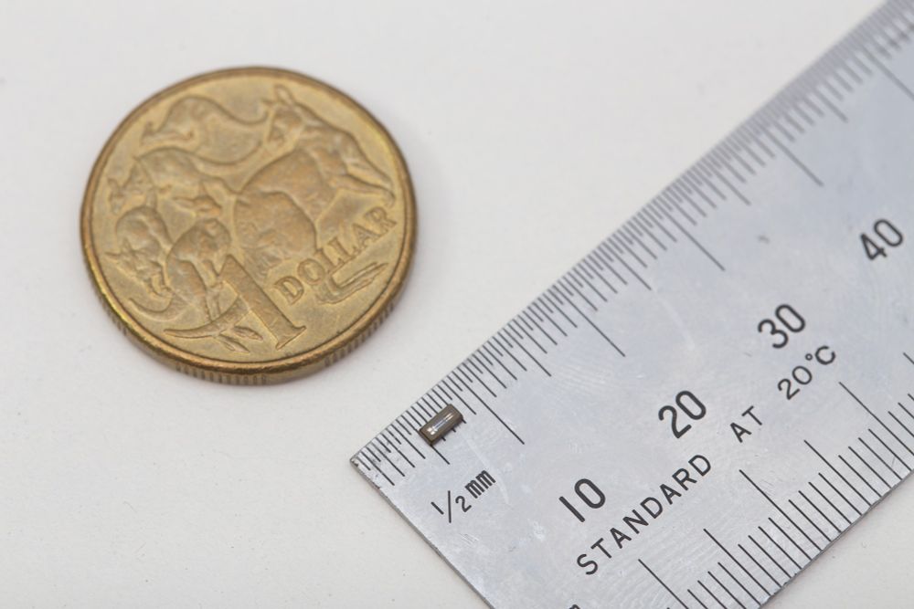 Australian dollar coin next to ruler. The ruler has a surface mount 32.768kHz crystal component, showing about 3mm in length.