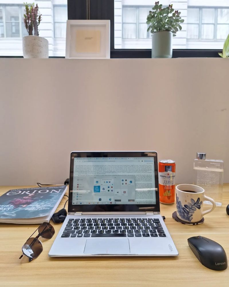 A laptop at a desk behind bright windows