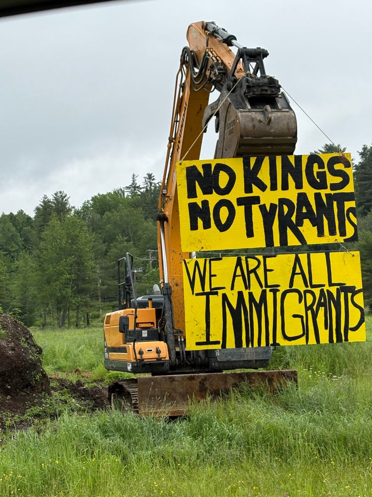 No kings sign hanging from an excavator in a field.