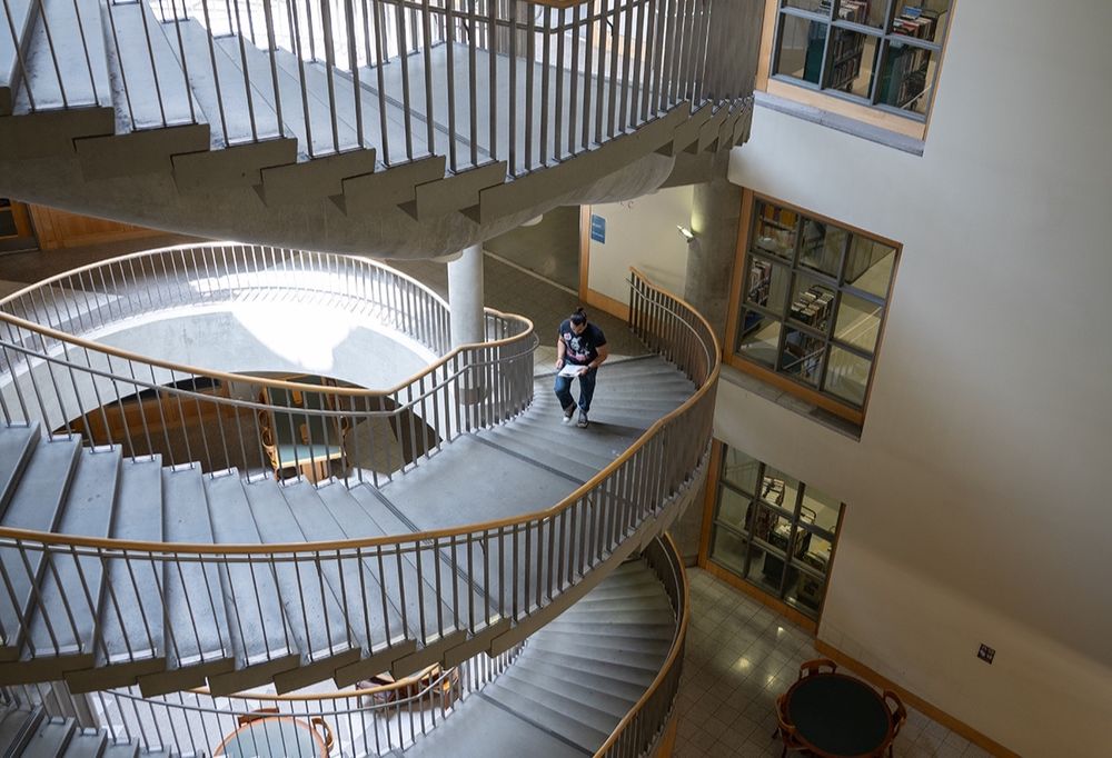 An individual walking down a spiral staircase inside a modern building with multiple levels and railings.