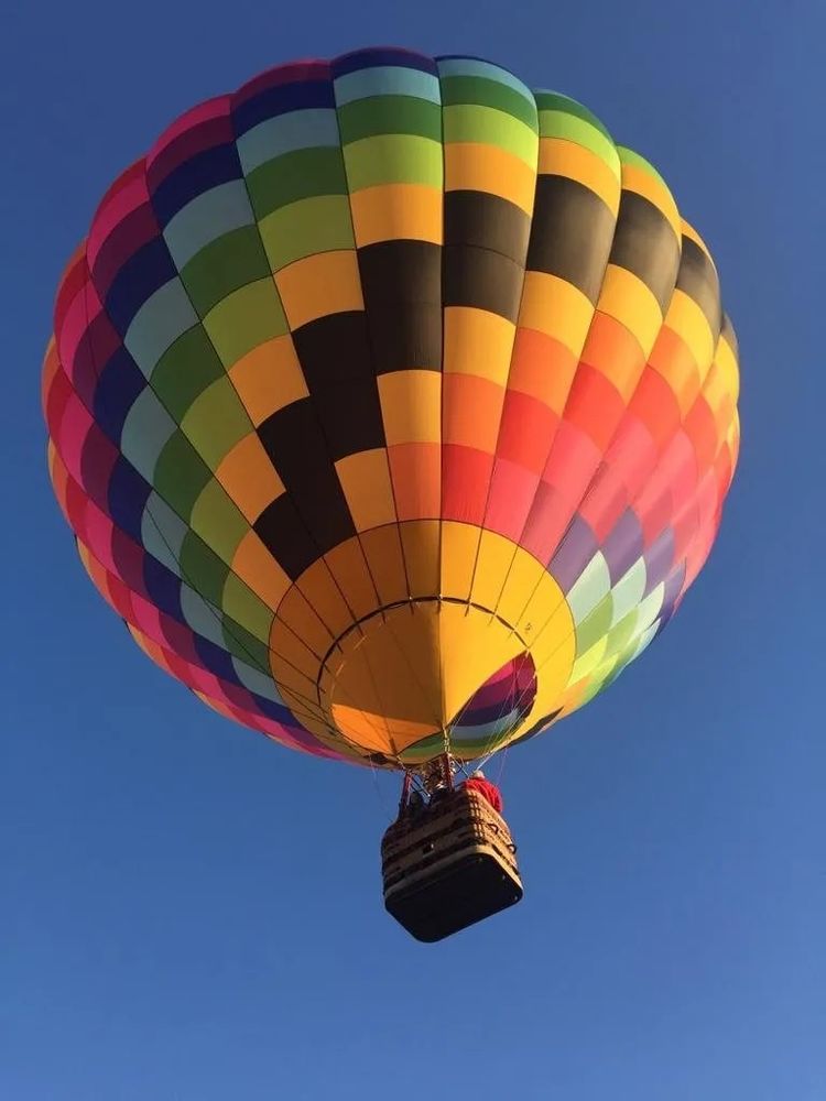 Photo d'une montgolfière multicolore dans le ciel bleu, vue du dessous. 