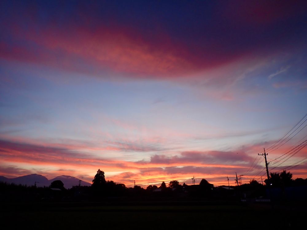 Morning scenery. Red-orange clouds up in the sky and orange clouds along the horizon. There is a wide opening between the clouds and blue sky is showing. Landscape in silhouette.