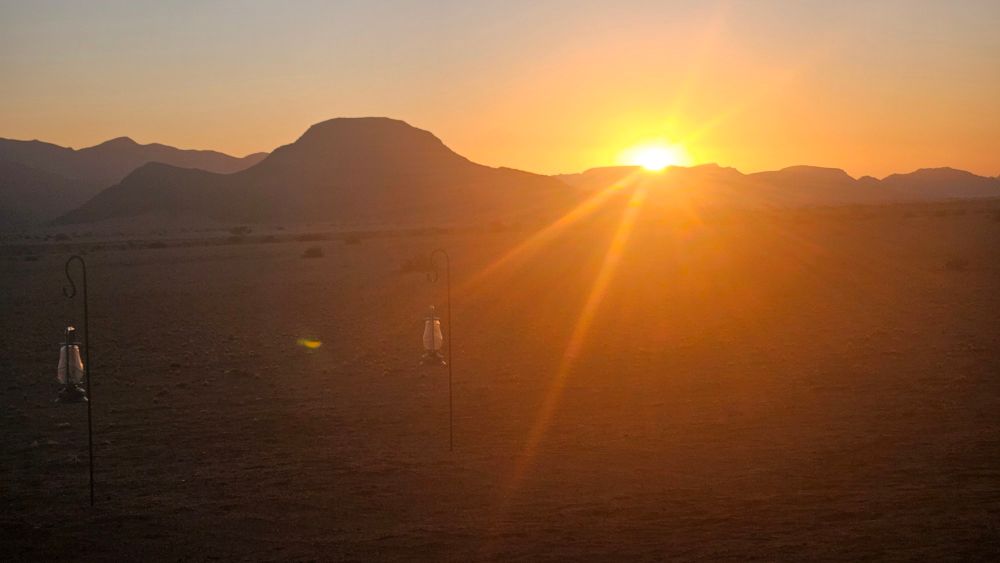 Sun rising over the horizon, cresting distant hills in the Namb desert.