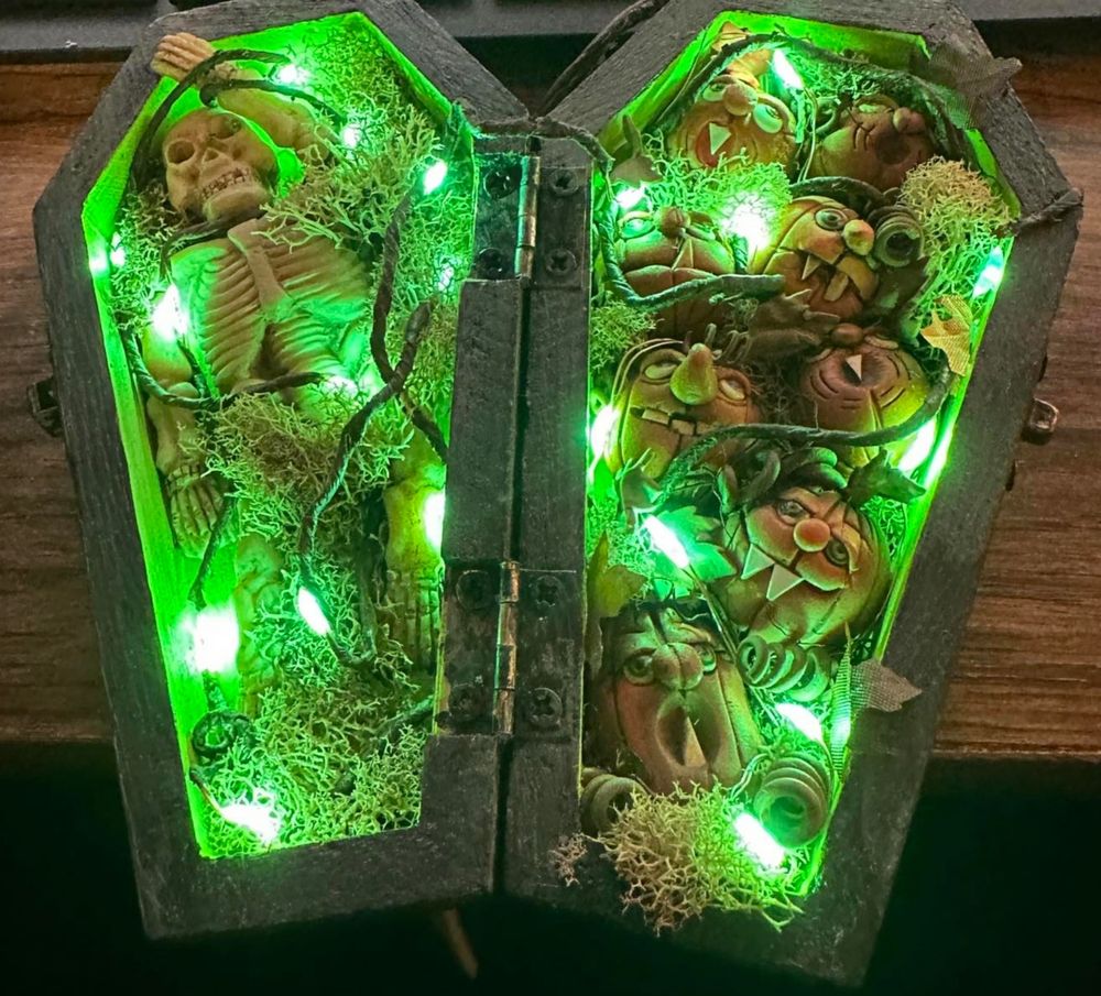 Small wood coffin with a resin skeleton on one side and vampire jack o'lanterns on the other with vines and moss.