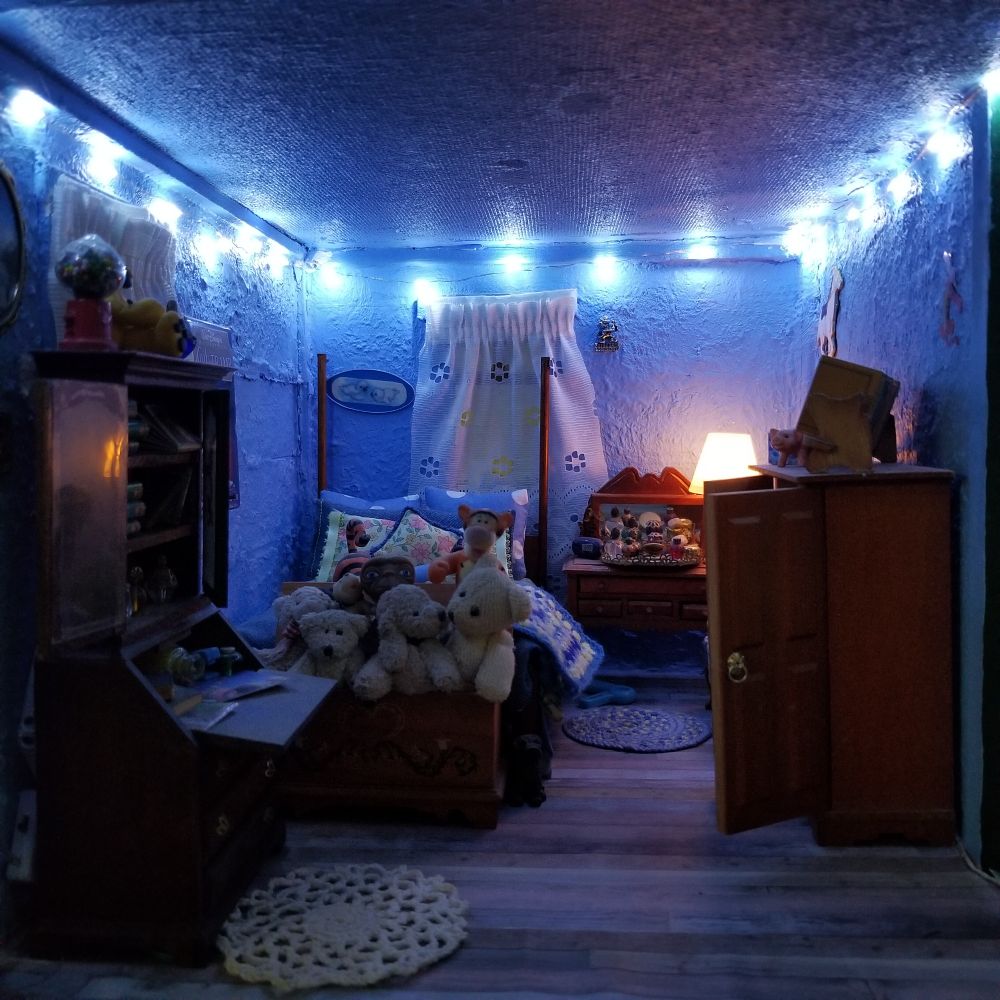 Full view of bedroom showing lights around ceiling, desk with hutch, 4 poster bed, trunk with stuffed animals, vanity table, comfy chair and wardrobe.