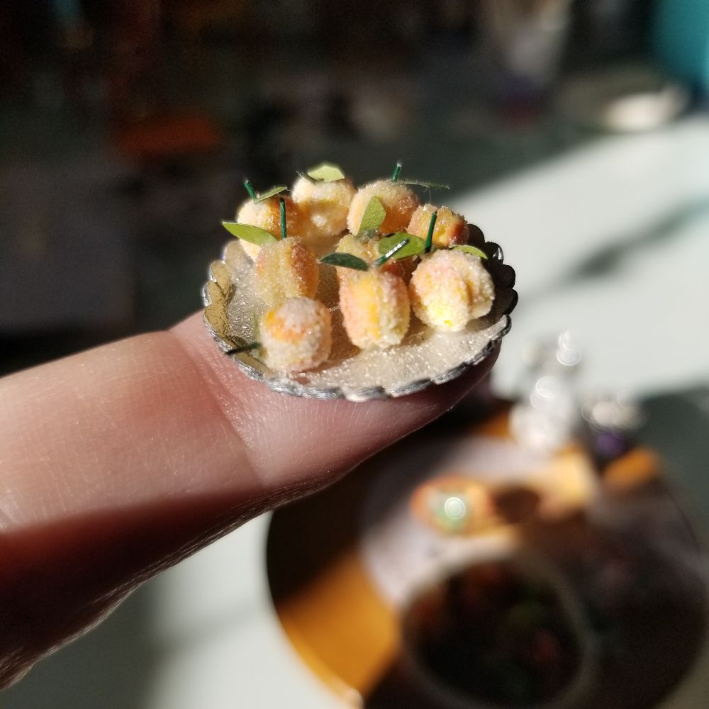 Finger holding silver foil tray of peach cookies (polymer clay).