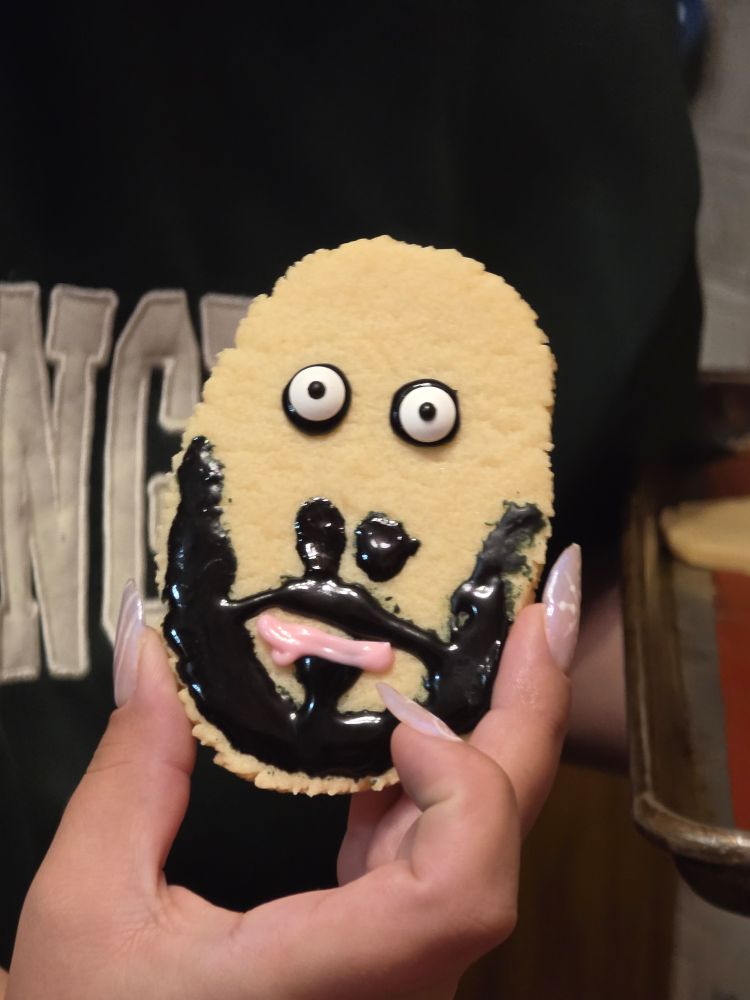a roundish sugar cookie with googly eyes and a sickly looking beard made from black icing